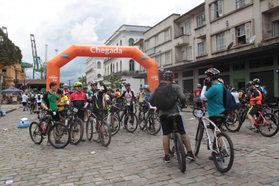 Ciclistas estão parados diante de um pórtico onde se lê Chegada. #Pracegover