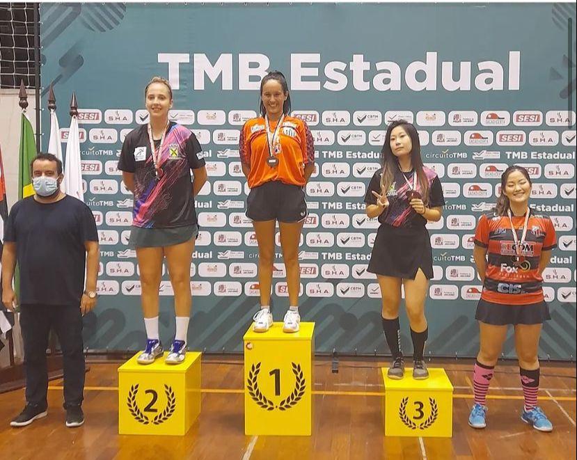 Maiza Mota está no lugar mais alto do pódio. A medalha está no peito. Do lado esquerdo, o segundo lugar, e do direito, o terceiro e quarto. #paratodosverem