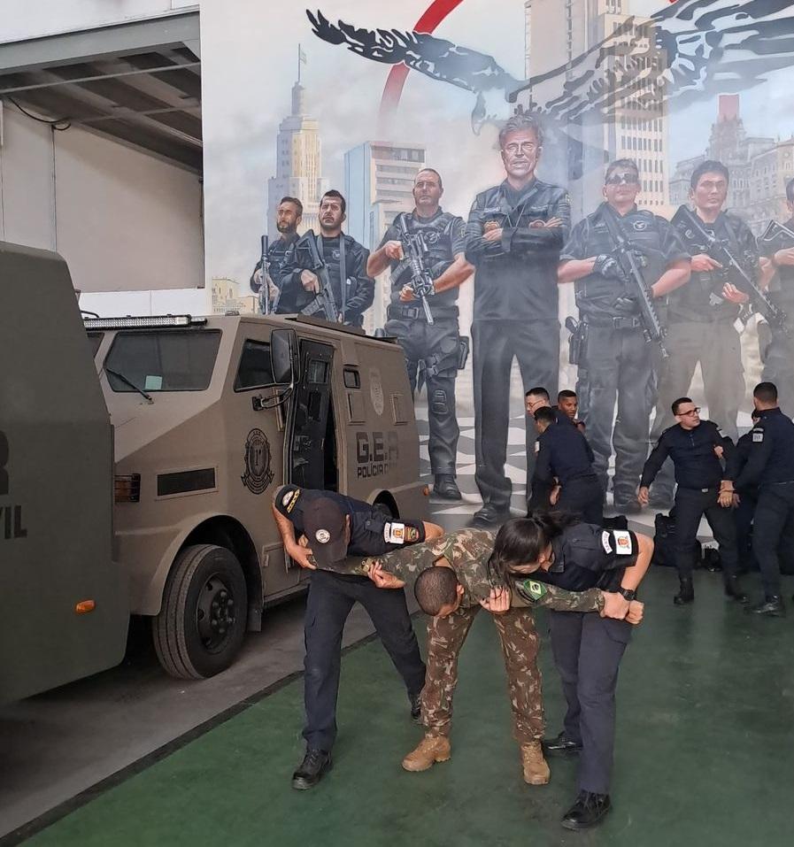 homem com roupa camuflada simula ação enquanto é contido por dois guardas. #paratodosverem 