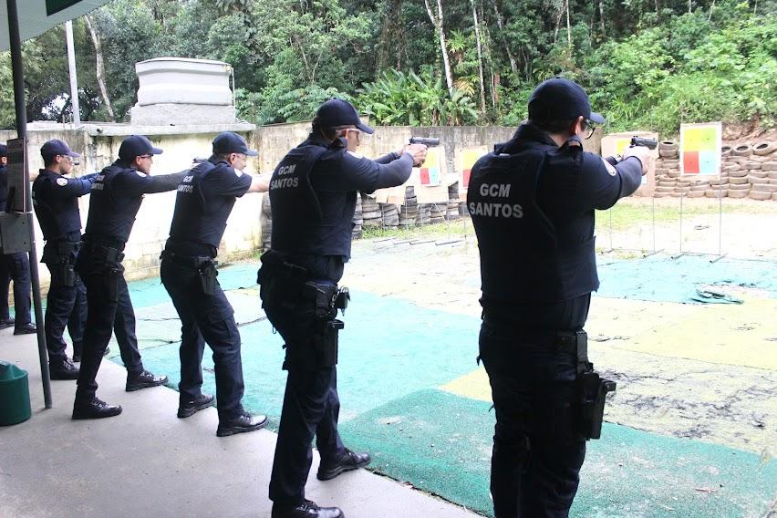 guardas estão enfileirados, todos segurando armas com mãos estendidas e apontando para alvos no fundo de uma espécie de quadra. #paratodosverem