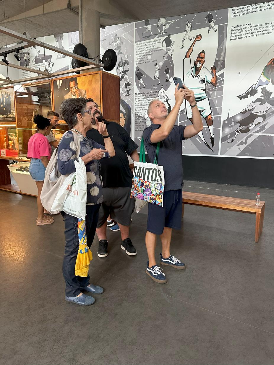 pessoas estão observando o interior do museu pelé. Um deles tira foto com celular. #paratodosverem 