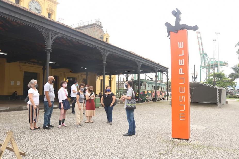 Pessoas ouvindo um guia na frente de estação #paratodosverem