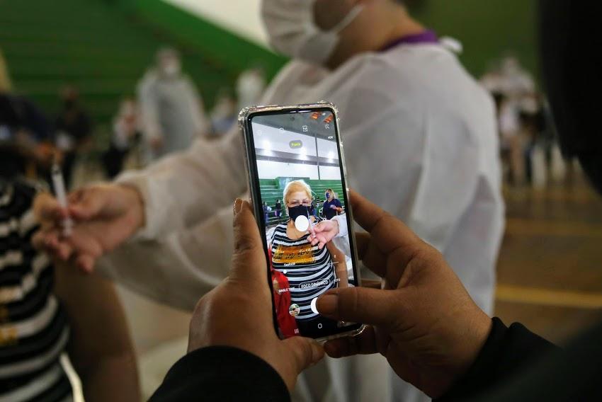 mãos seguram smartphone fotografando pessoa diante de agulha. #paratodosverem