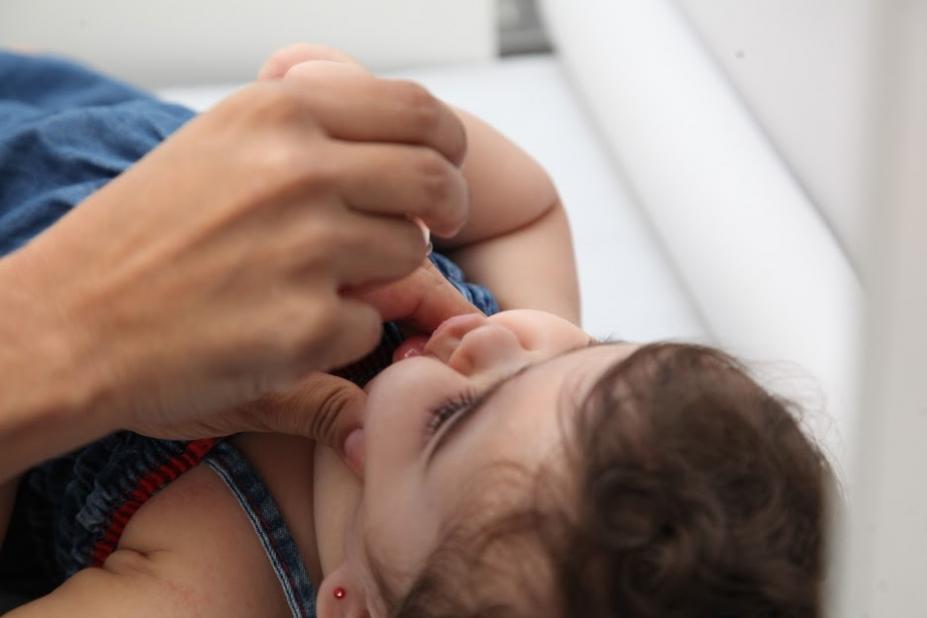 mão pinga gota da vacina sabin na boquinha de uma criança. #paratodoverem