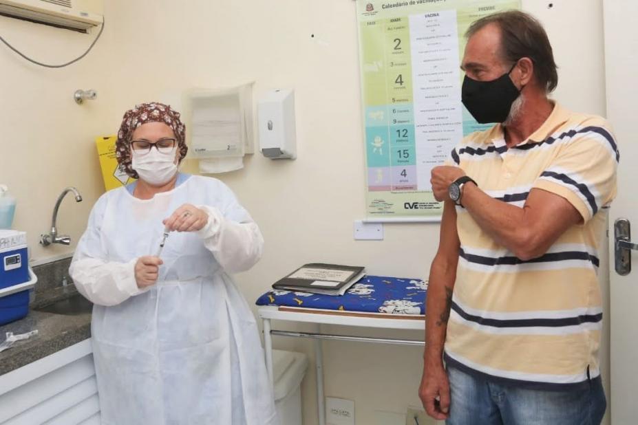 mulher prepara vacina enquanto homem levanta manga de camiseta para ser imunizado. #paratodosverem