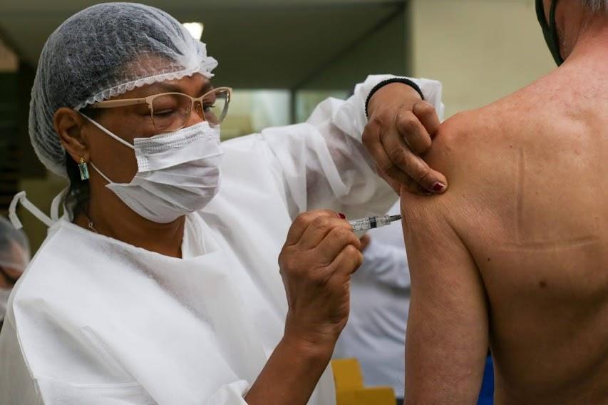 mulher usando avental, touca e máscara vacina homem. #paratodosverem