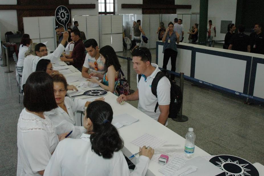 balção de atendimento montado em salão, com atendentes de um lado e turistas de outro. Sobre o balcão há papéis. #paratodosverem