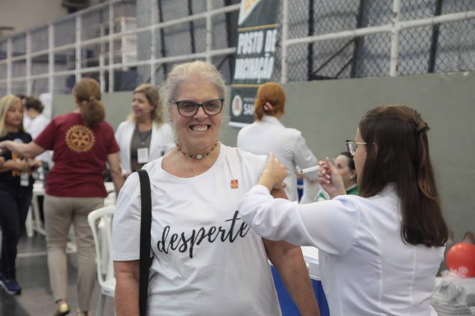 Mulher com camisa branca escrita Desperte recebe vacinação de profissional de saúde. #pratodosverem