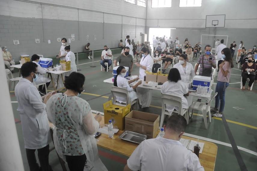 ginásio esportivo com pessoas espalhadas para vacinar e serem vacinadas. #paratodosverem