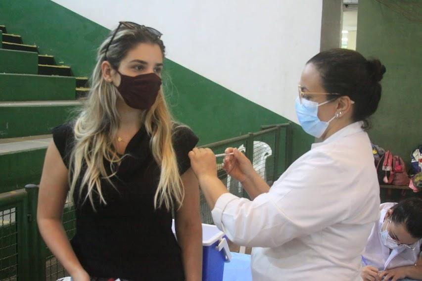 Mulher é vacina por profissional de saúde em ginásio poliesportivo. #pracegover