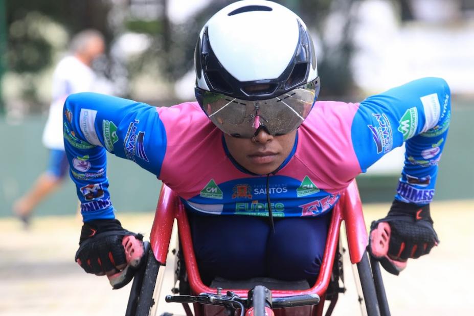 Paratleta, de óculos e capacete, corre em cadeira de rodas. #paratodosverem