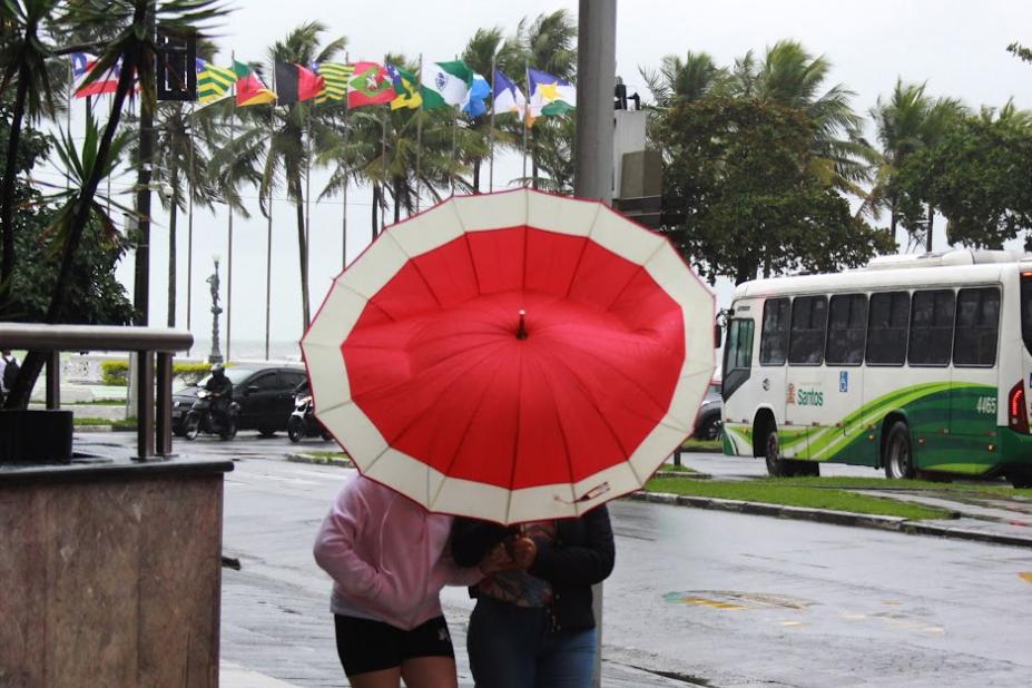 duas mulheres estão sob guarda-chuva que está envergado devido ao vento. #paratodosverem