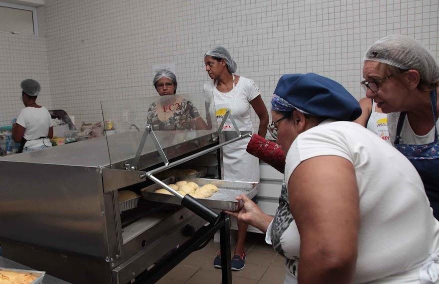 Mulheres colocam alimento no forno industrial. #pracegover