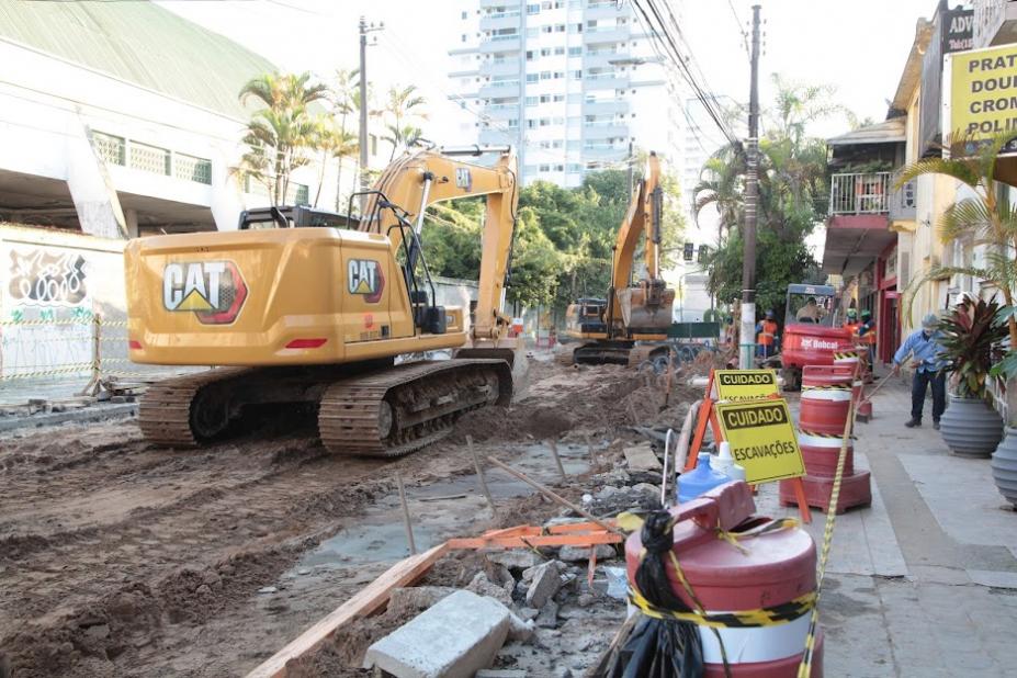 Retroescavadeira operando em rua com cones de interdição em volta. #pracegover