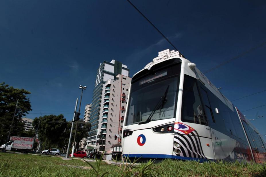 Veículo leve sobre trilhos em primeiro plano com prédios ao fundo. 