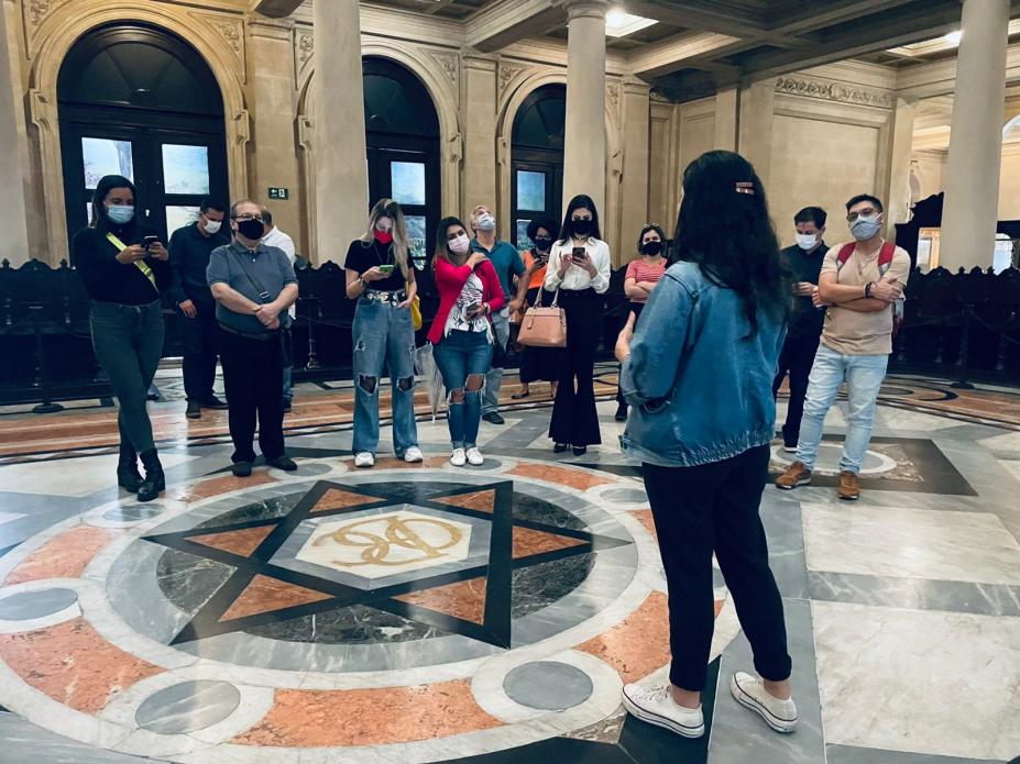salão do pregão da bolsa oficial do café, com pessoas em pé atentas a uma guia que está de costas para a foto. #paratodosverem