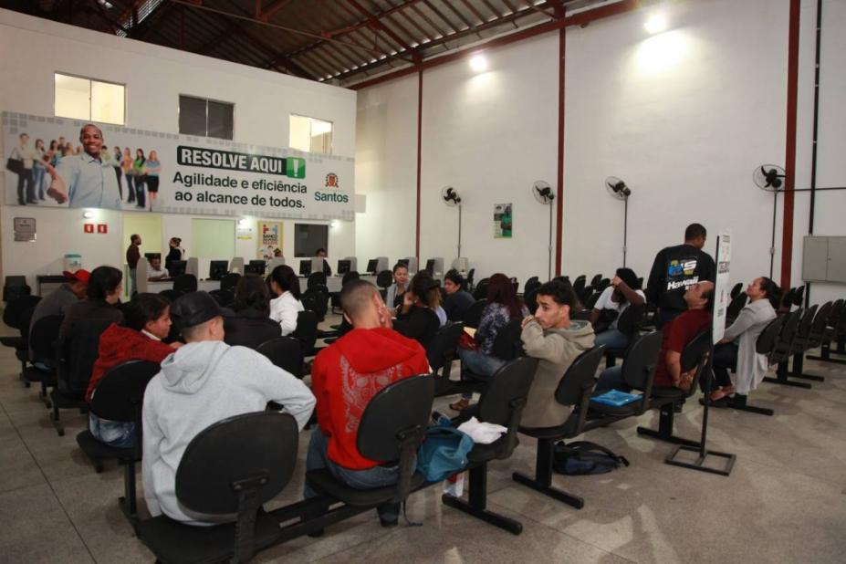 Cerca de 20 pessoas sentadas em cadeiras aquardam atendimento à frente de cartaz do programa Resolve Aqui