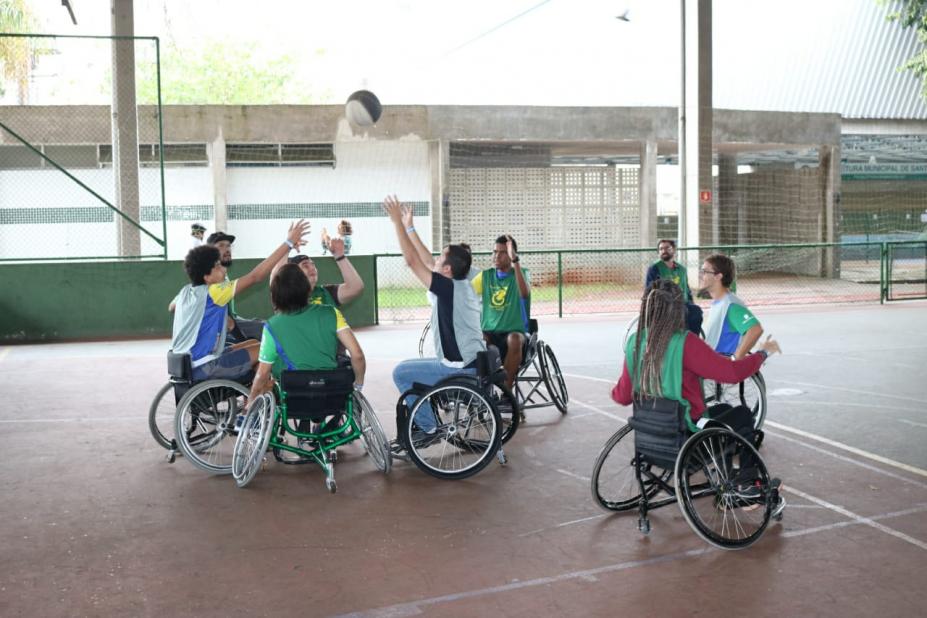 Seis jovens em cadeira de rodas erguem as mãos em disputa de bola de basquete dentro de quadra