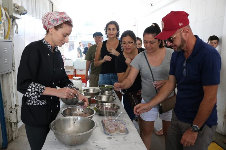 Mulher de uniforme preto serve ceviche a fila de pessoa