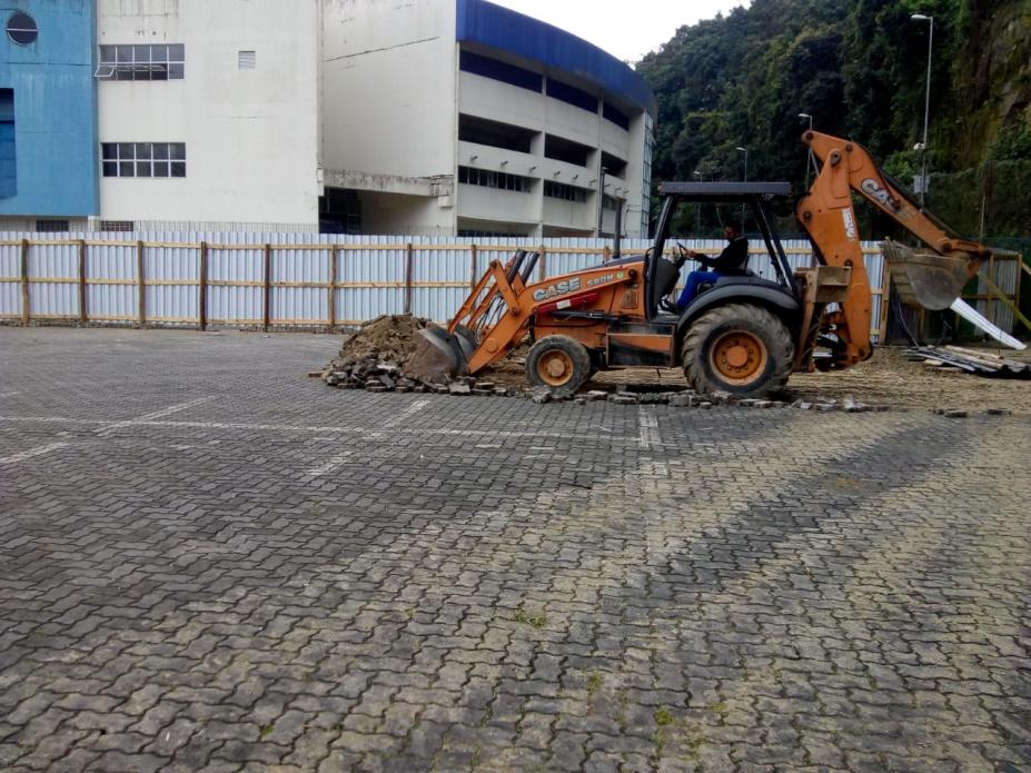 Trator remove piso remanescente de área descoberta. Ao fundo se vê o prédio da Arena Santos. #Pracegover