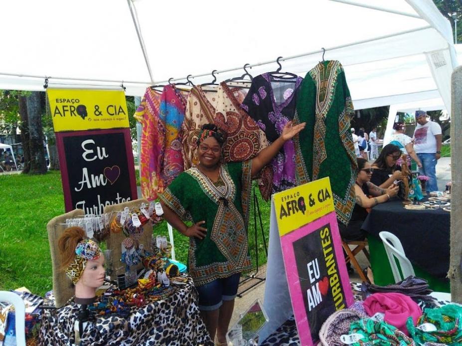Mulher mostra barraca com vários produtos da cultura afro #paratodosverem