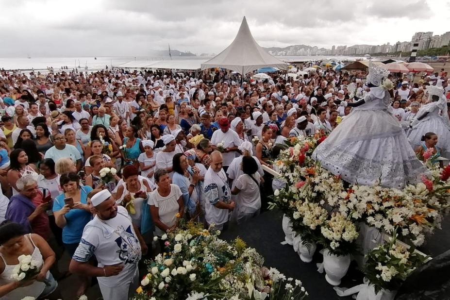 #pracegover na areia da praia, milhares de pessoas observam estátua de Iemanjá exposta sobre patamar