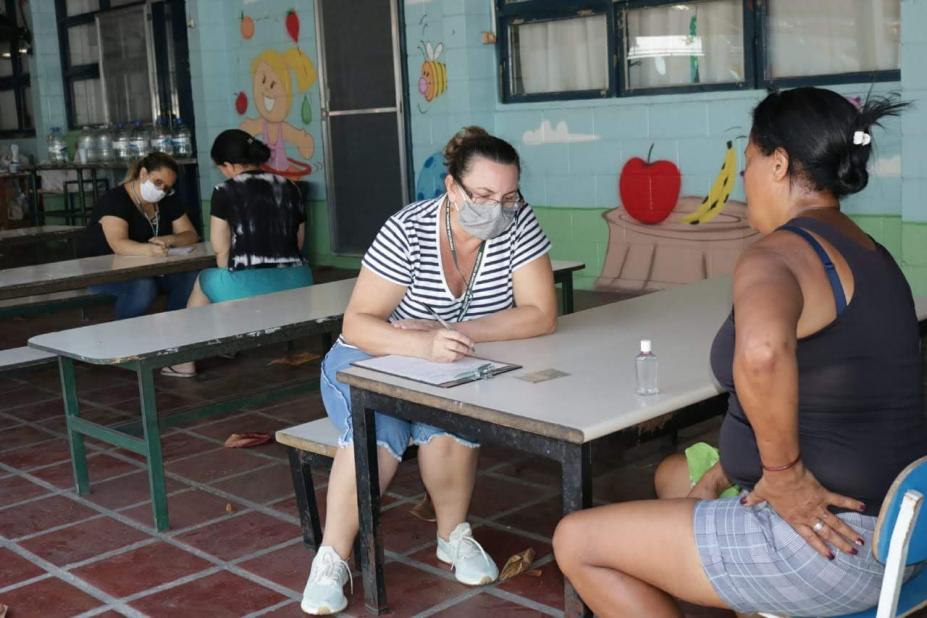 mulheres são atendidas por servidoras de máscara em mesas da escola #paratodosverem 