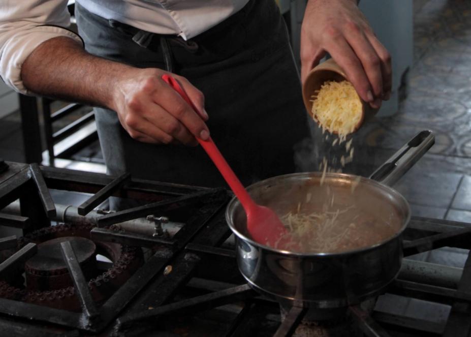 #fpracegover oto mostra homem adicionando tempero em panela com feijão sobre o fogão