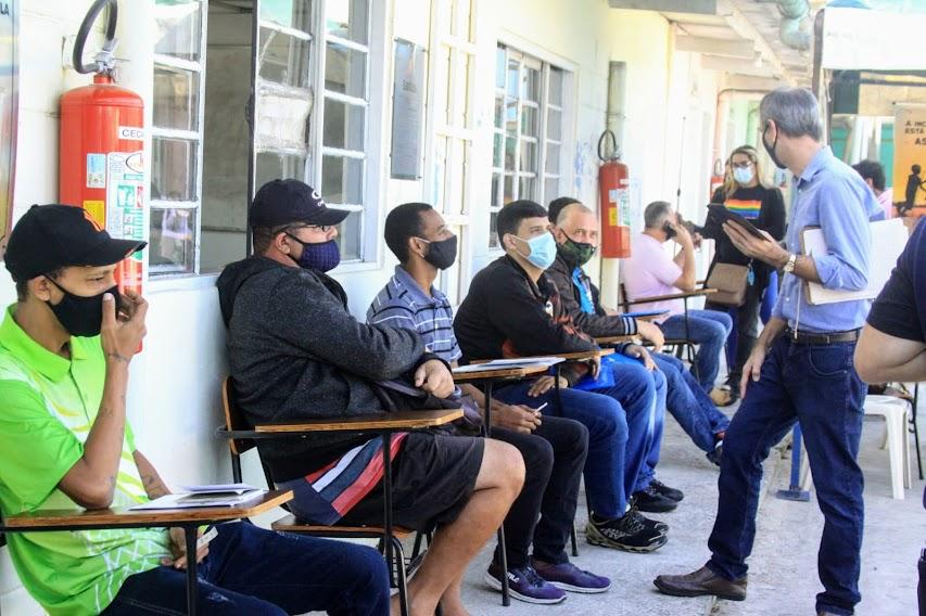 pessoas aguardam sentadas em pátio de escola #paratodosverem