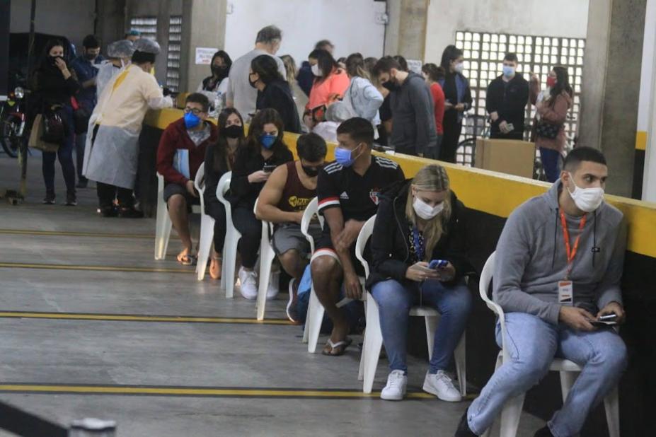 Jovens sentados enfileirado aguardando a vacinação. #paratodosverem