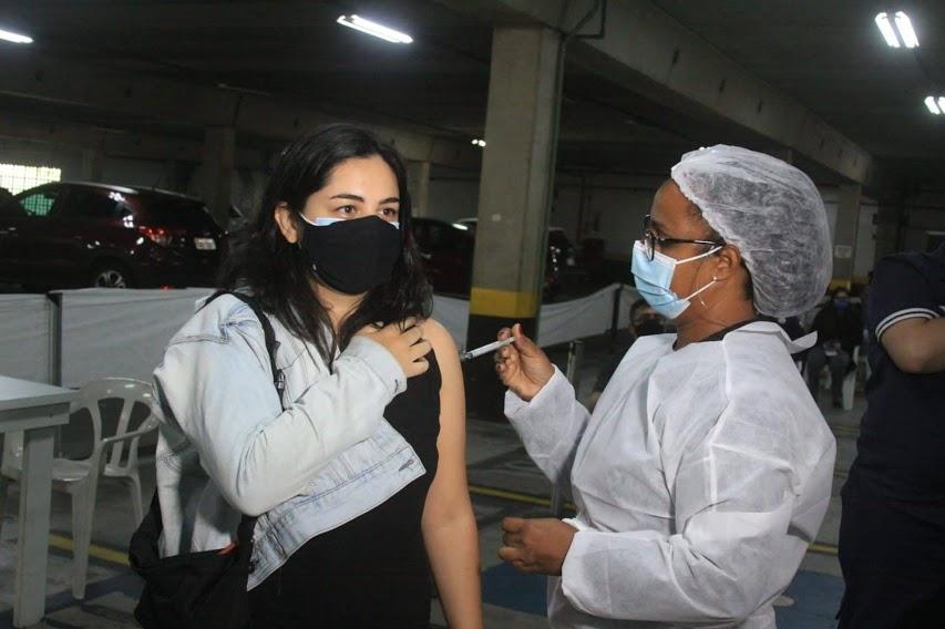 Mulher tem vacina aplicada no seu braço por enfermeira. #paratodosverem