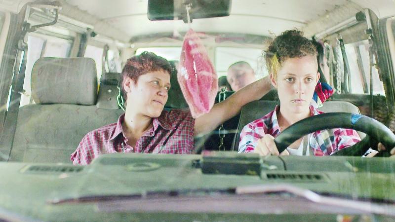 Em cena do filme, a mulher está com a mão atrás da mulher que está dirigindo com cara séria #paratodosverem