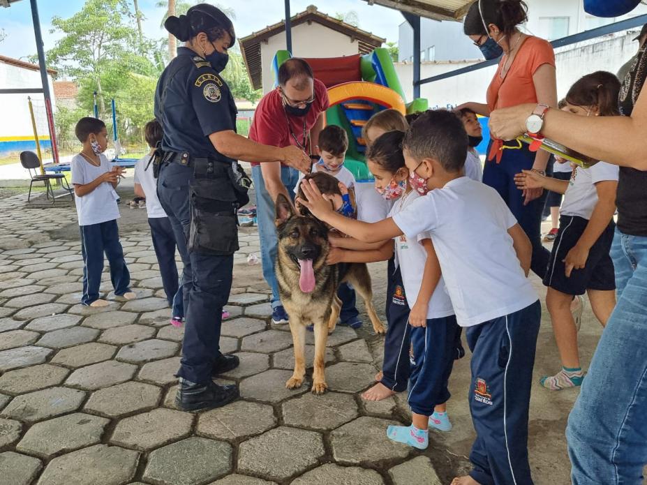 Crianças passam a mão em cachorro do canil da guarda com agente ao lado #paratodosverem