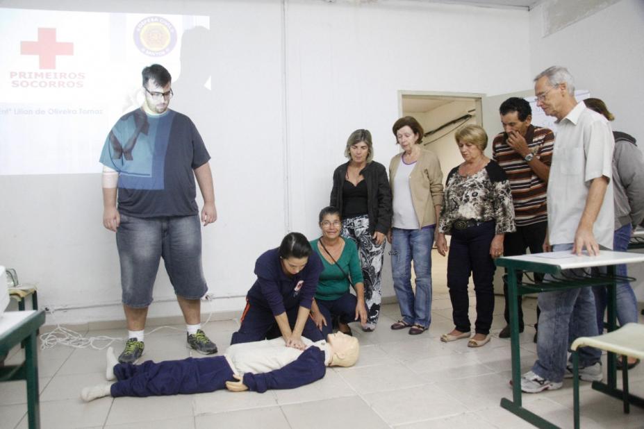 instrutora simula socorro em boneco no chão, pessoas olhando, sala fechada