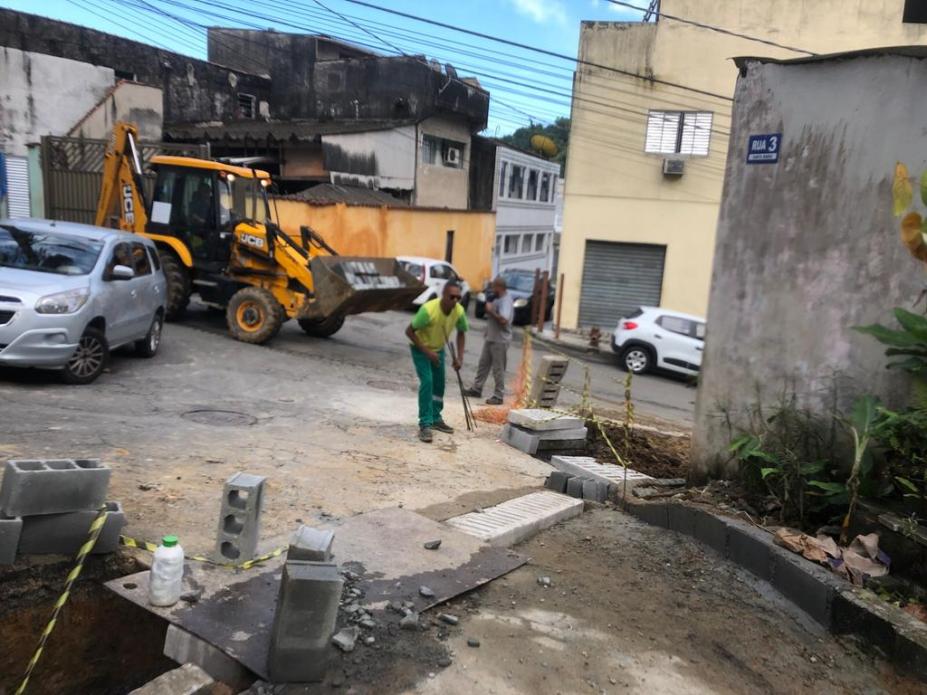 trabalhador realiza obra em rua , escavadeira ao fundo, blocos de concreto #paratodosverem