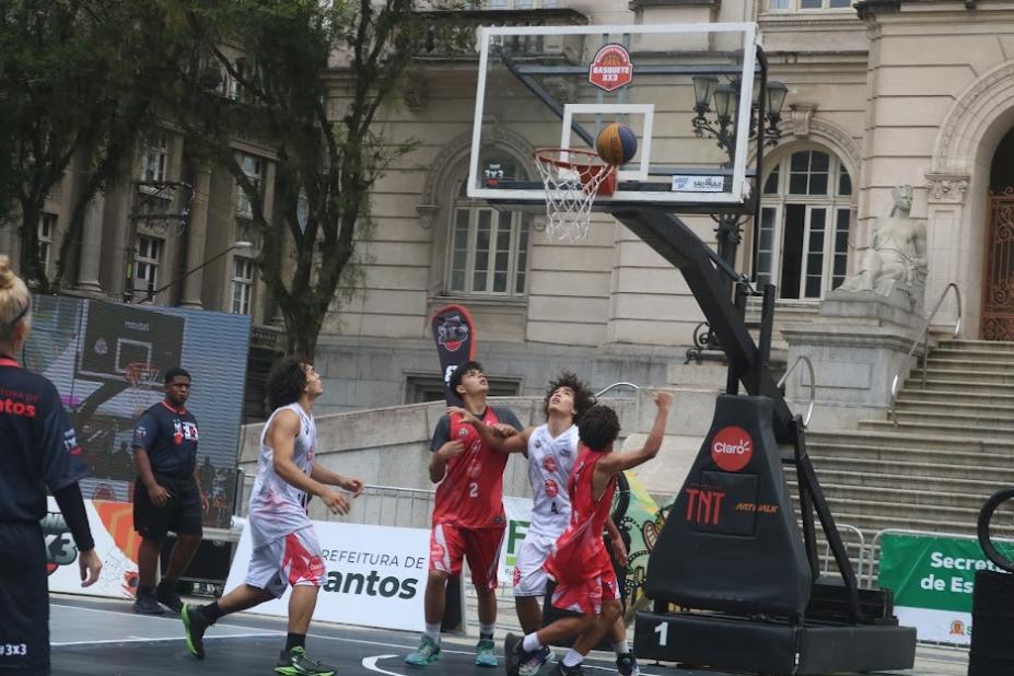 atletas jogam basquete em frente a uma cesta , em praça #paratodosverem