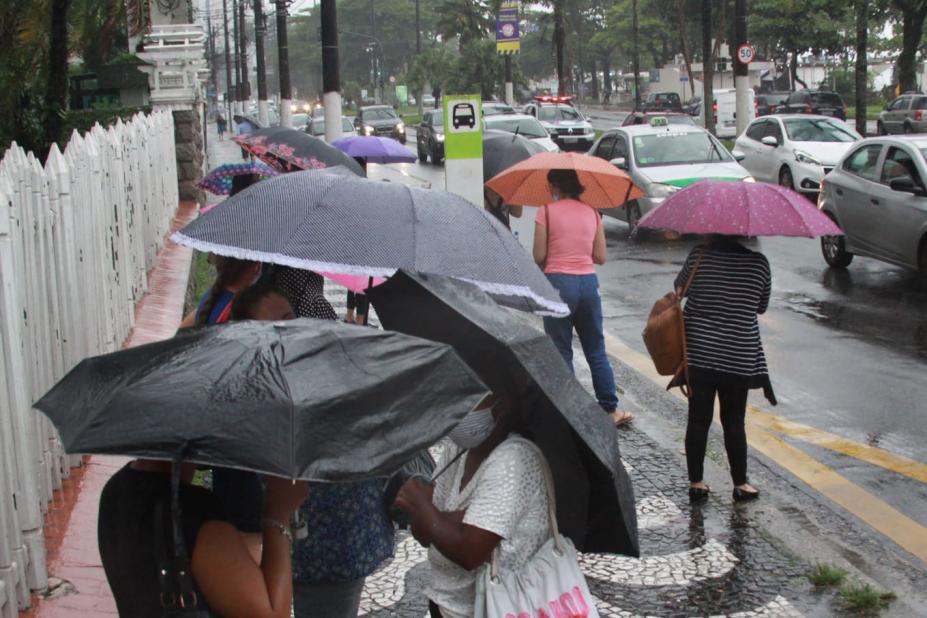 pessoas de guarda chuva em ponto de ônibus com vários carros passando na avenida #paratodosverem