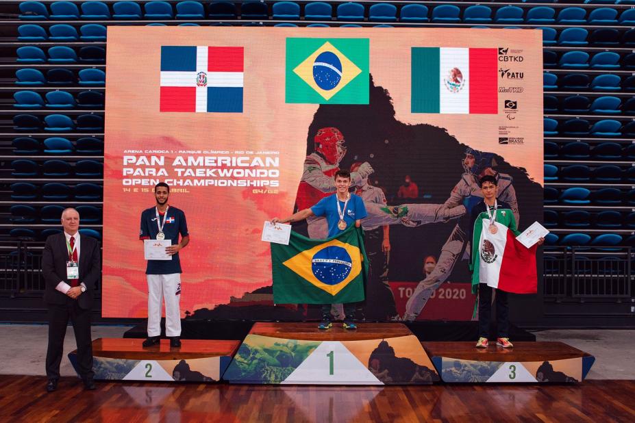 atletas no pódio com medalhas e segurando bandeira #paratodosverem