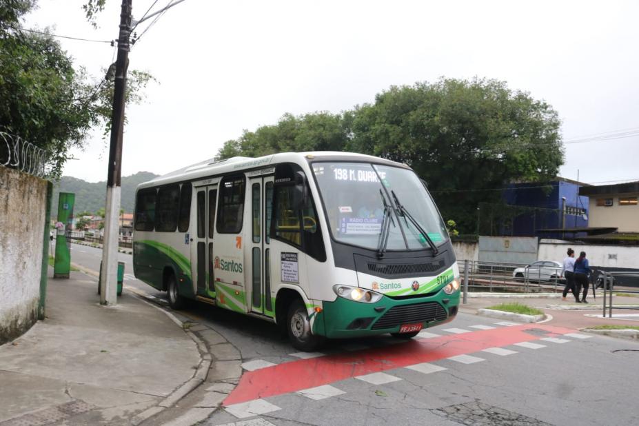 ônibus nas cores verde e branca passando na rua perto de um poste #paratodosverem