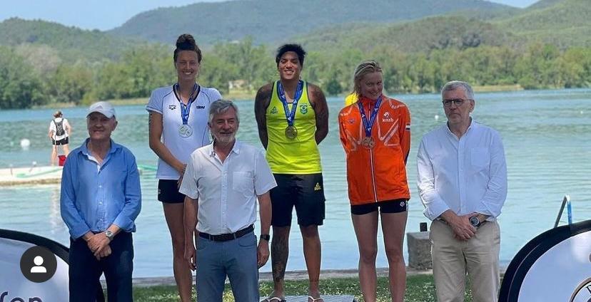 atletas no pódio com medalhas e rio ao fundo #paratodosverem