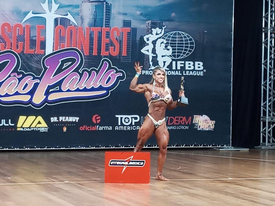 atleta exibe troféu no palco #paratodosverem