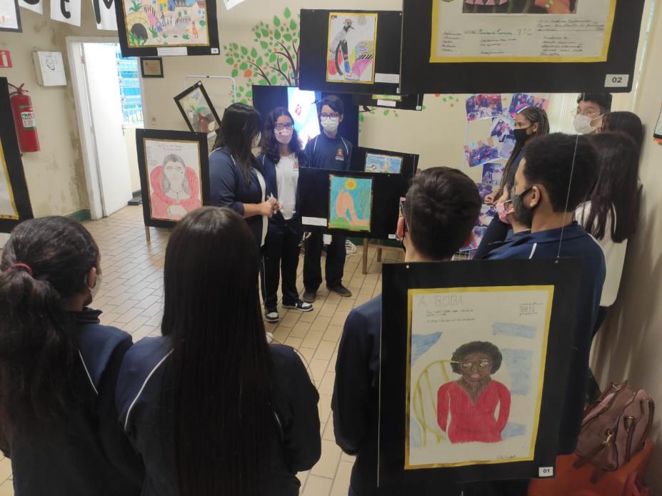 alunos em sala com várias obras em exposição penduradas #paratodosverem