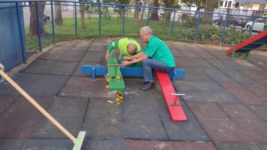 funcionários consertam brinquedo em playground #paratodosverem