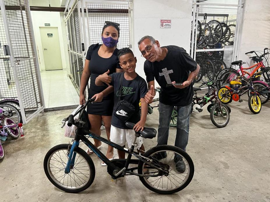 mãe e pai ao lado de filho que segura a bicicleta #paratodosverem