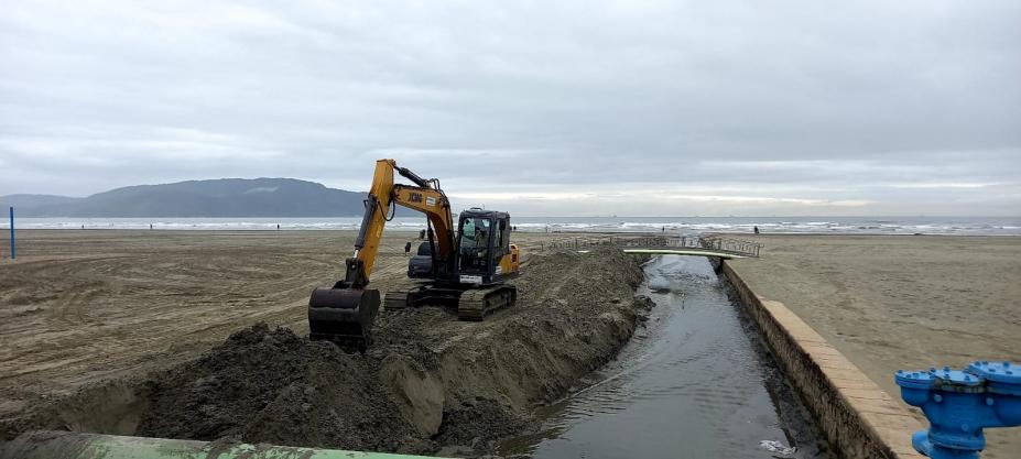 retroescavadeira retira areia ao lado de canal na praia #paratodosverem