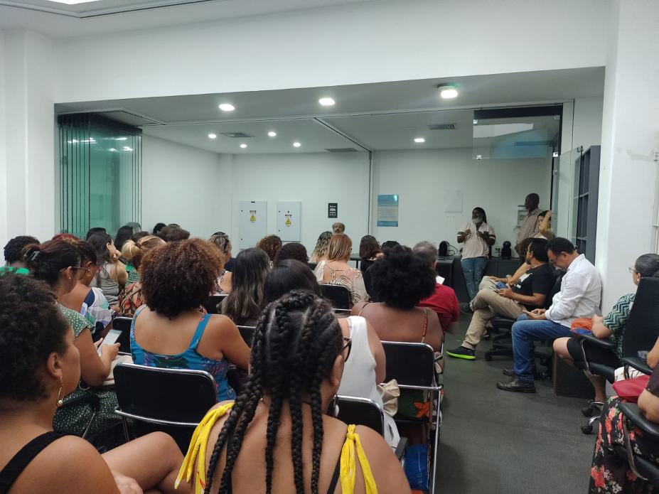 auditório lotado com pessoas sentadas. Ao fundo, um homem faz palestra. #paratodosverem 