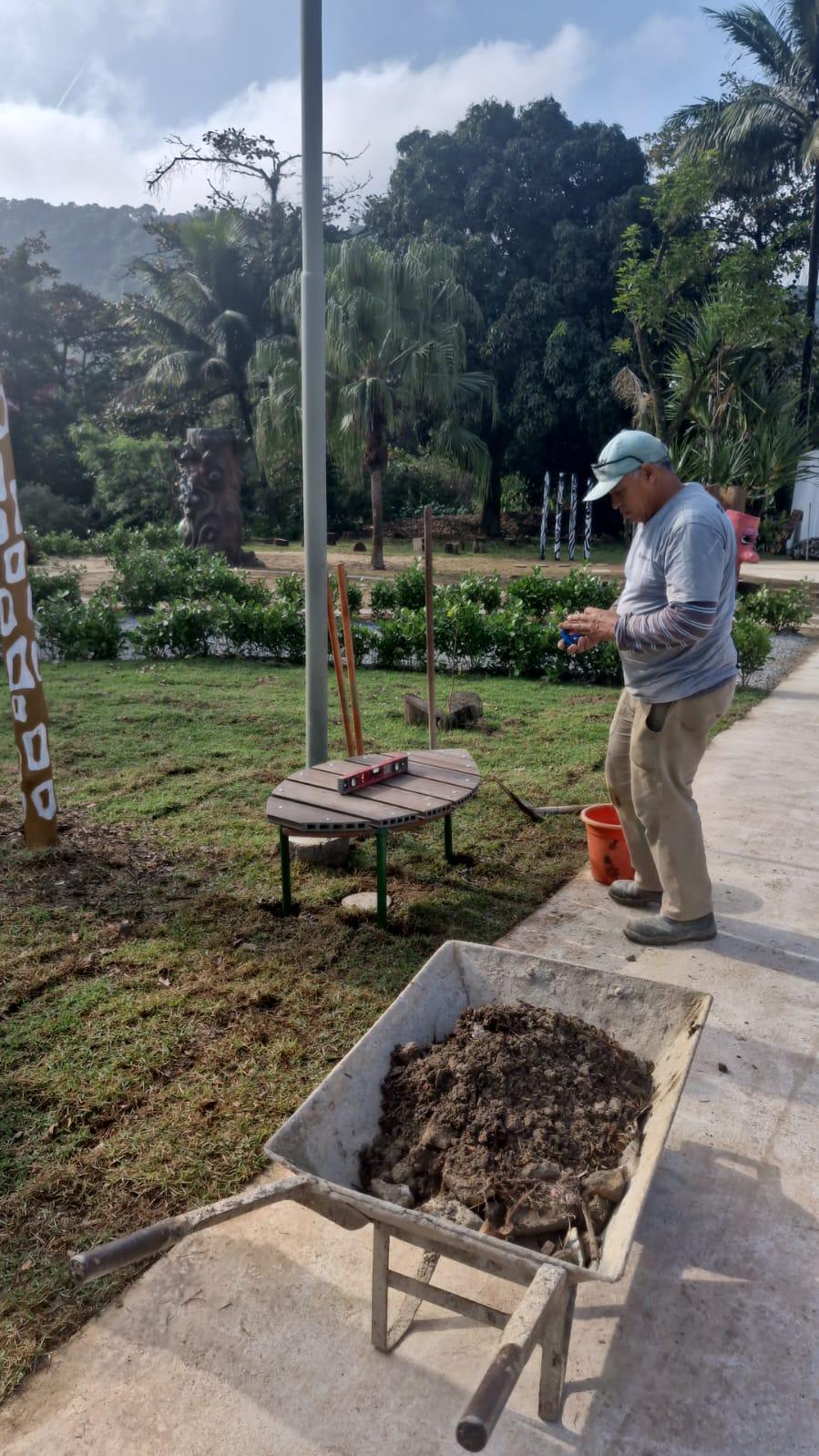 homens instala banco de madeira feito com material reaproveitado. Em volta há grande área verde. #paratodosverem 
