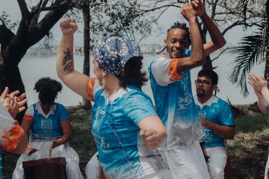 roda de dança com foco em casal que se movimenta no centro com os braços para cima. #paratodosverem 