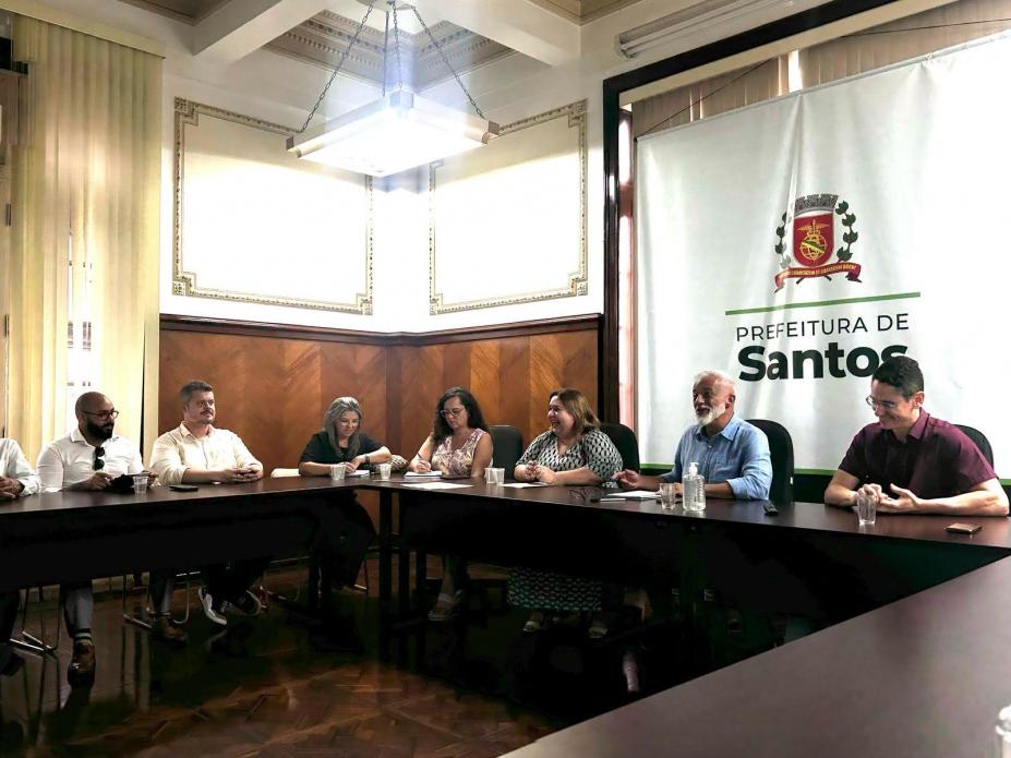 pessoas conversam reunidas em torno de mesa. #paratodosverem