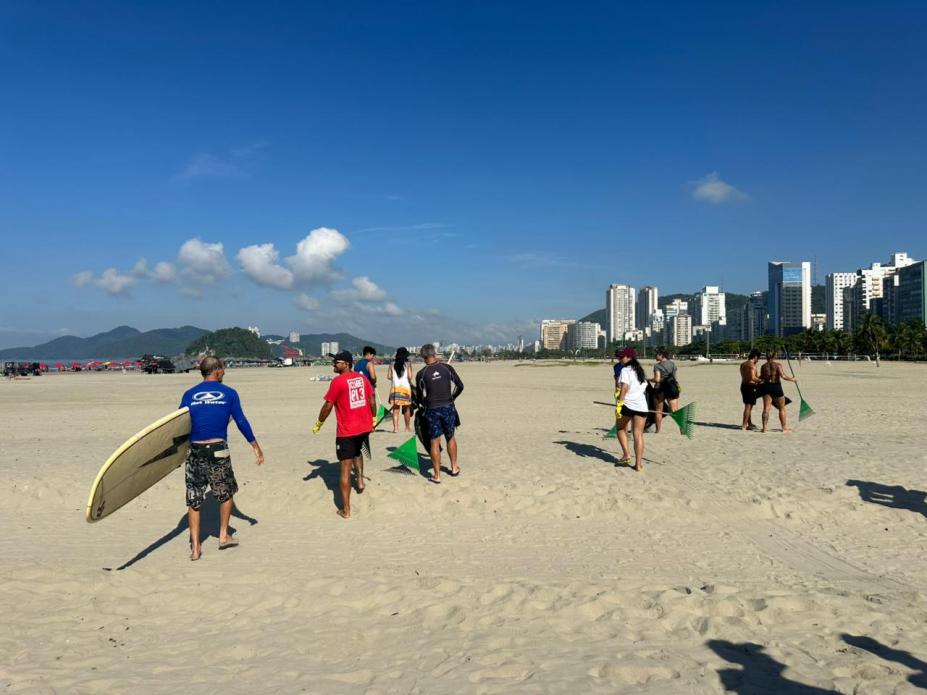 pessoas caminham pela faixa de areia para recolher detritos. #paratodosverem
